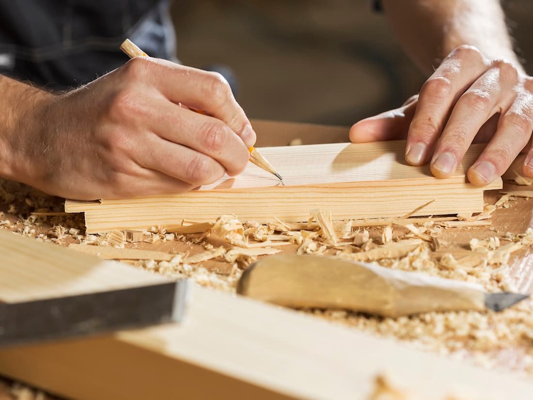 Hands marking a cut line on a length of timber with a pencil