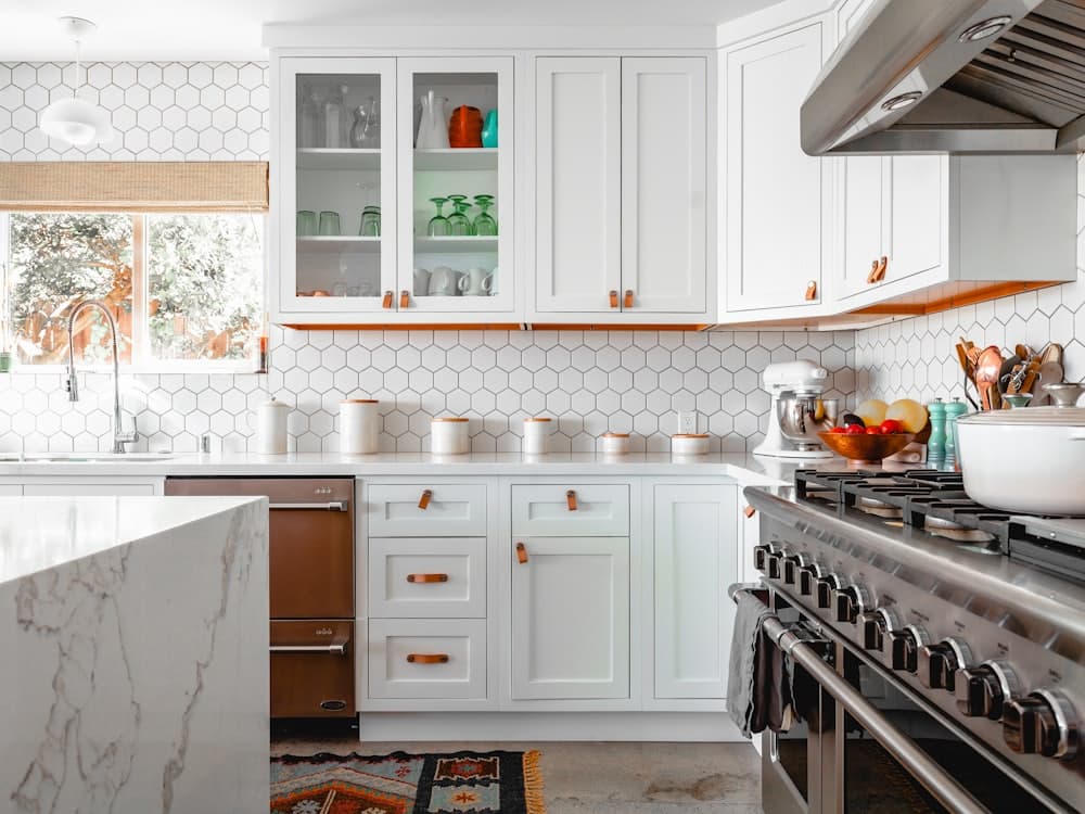 A white kitchen with a hexagonal tile backsplash and marble island